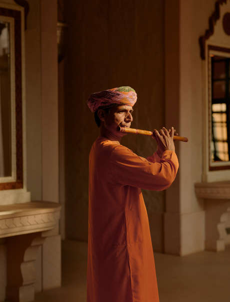 Musician playing traditional instrument at Amanbagh, dressed in rust-coloured robes.
