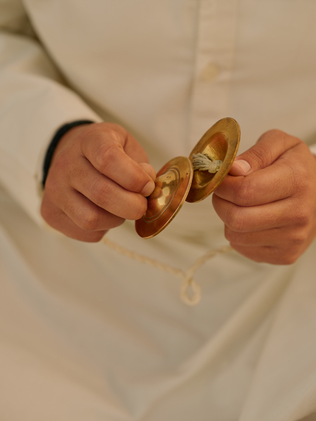 Hands holding brass cymbals during a yoga session at Amanbagh.