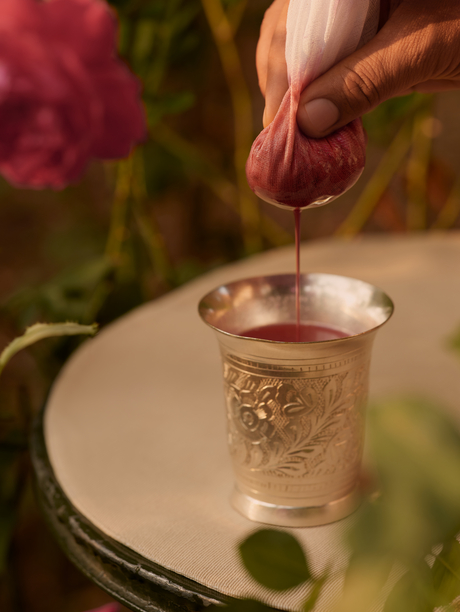 Hand holding a rose petal above a glass of water at Aman-i-Khas, India.
