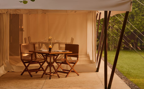 Dining pavilion at Aman-i-Khas with wooden table and chairs opening to manicured lawns.