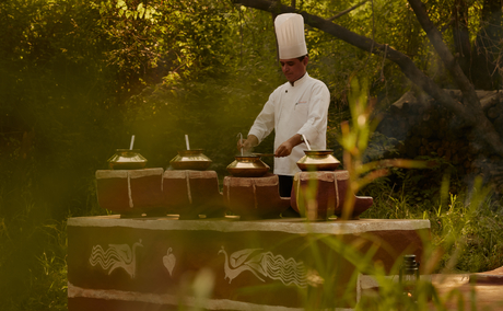 Chef preparing a meal at an outdoor dining table surrounded by greenery at Aman-i-Khas, India.