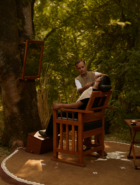 A guest sits alone in a wooden chair beneath towering trees at Aman-i-Khas, surrounded by dappled sunlight filtering through the canopy.