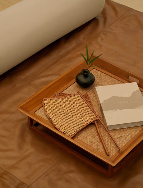 Wooden tray with woven details, small plant and open book inside an Aman-i-Khas tent.