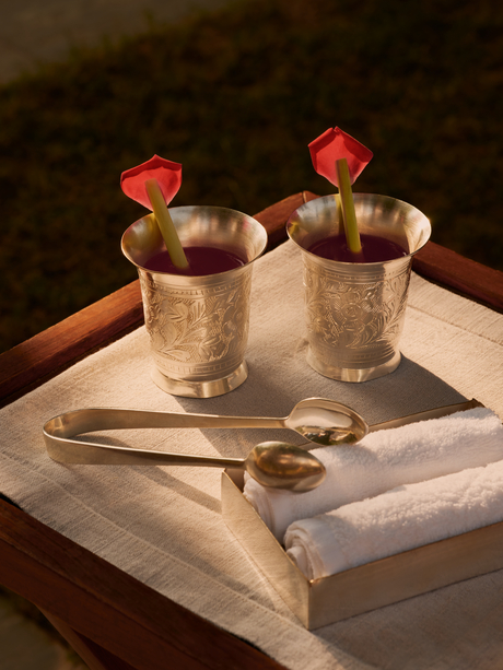 Welcome drinks served in gold vessels at Aman-i-Khas, garnished with red flowers and presented on marble.