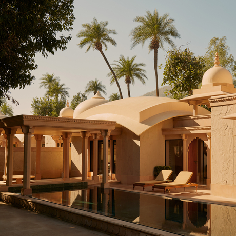 Pool pavilion at Amanbagh with terracotta dome and wooden columns, framed by palm trees.