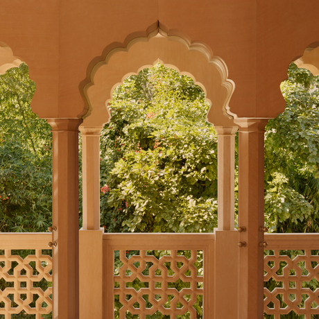 Terrace of Haveli Suite with arched doorway and carved lattice screens overlooking garden at Amanbagh, India.