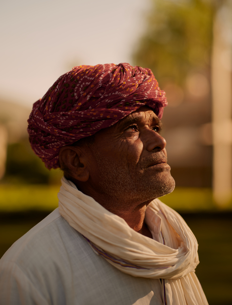 Woman wearing burgundy turban and cream scarf at Amanbagh, looking toward distant landscape.