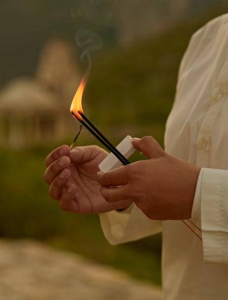 Hands holding a lit incense stick during a yoga session at Amanbagh.