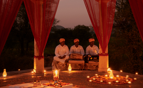 Candlelit chhatri dinner at Amanbagh, with guests seated beneath red silk drapes surrounded by flickering flames.