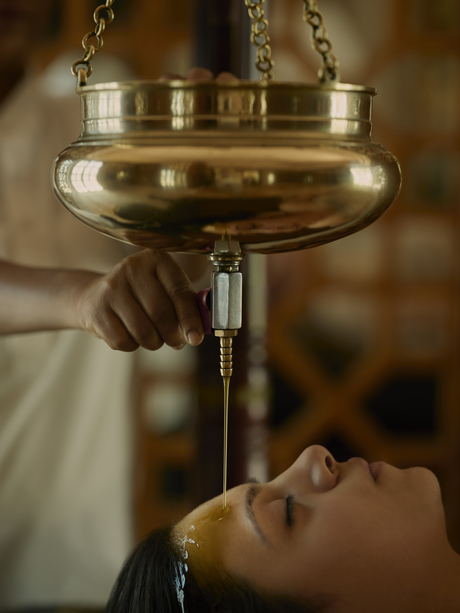 Therapist pouring warm oil over guest's face during Ayurvedic treatment at Amanbagh spa.
