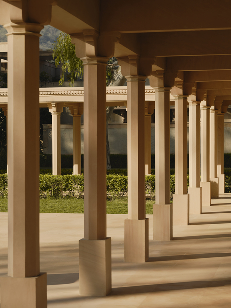 Colonnade walkway at Amanbagh with stone columns casting shadows, opening to gardens beyond.
