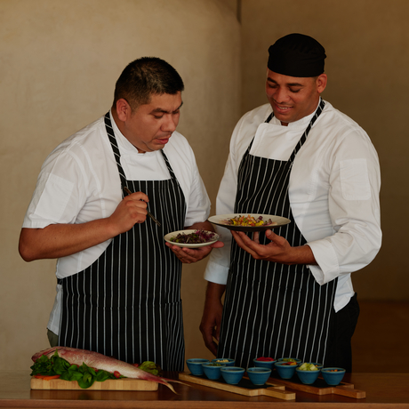 Two chefs in striped aprons prepare ingredients at Amanera's dining venue.
