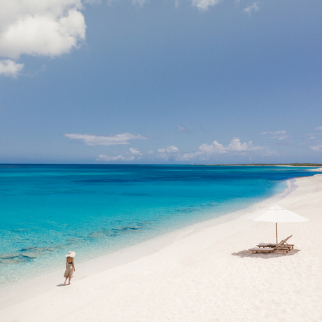 Turquoise waters and white sand beach at Amanyara, with a guest wading in the shallows and a wooden dhoni boat nearby.