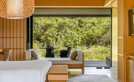 Mori Suite bedroom at Amanemu resort with view of Japanese woodland through floor-to-ceiling window.