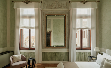 Palazzo Stanza bedroom at Aman Venice, with pale green walls, tall windows and a central mirror.
