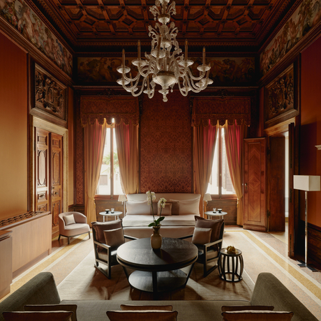 Sansovino Stanza bedroom at Aman Venice, featuring terracotta walls, chandelier, and classical furnishings.