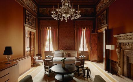Sansovino Stanza bedroom at Aman Venice, featuring terracotta walls, chandelier, and period furnishings.
