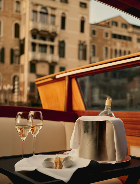 Man pouring Prosecco into a glass on a Venice boat, with historic palazzos reflected in the water behind.