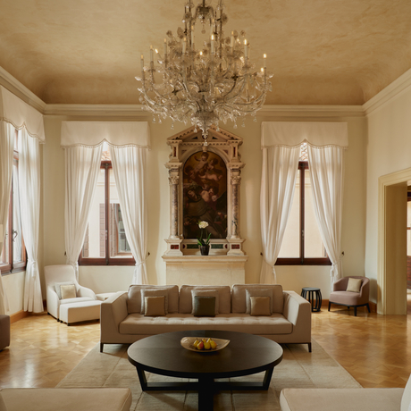 Living area in Coccina's apartment at Aman Venice, featuring a crystal chandelier, tall windows and classical furnishings.