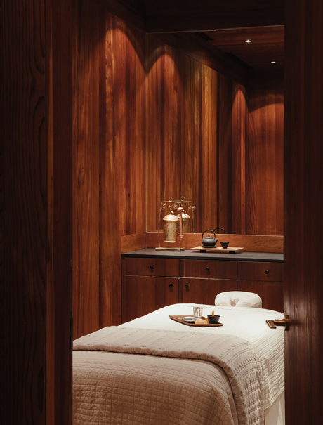 Spa treatment room at Amangani with warm wooden walls and a massage bed draped in cream linens.