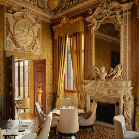 Ornate principal bedroom at Aman Venice with gilded walls, fireplace, and classical architectural details.
