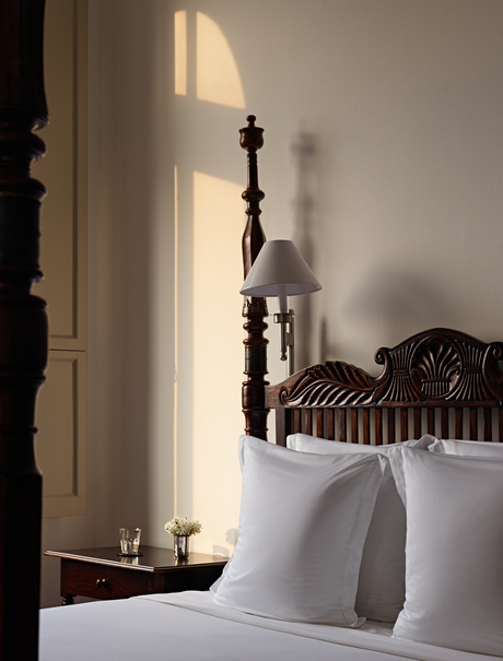 Sunlight streams through a sheer curtain beside a principal bedroom at Amangalla, illuminating a wooden cross on the bedside table.