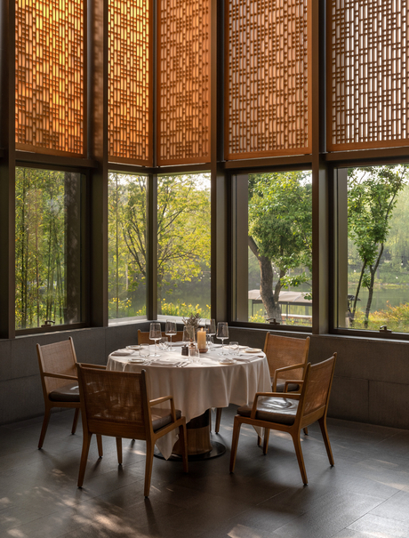 Dining area at Amanyangyun with round table, wooden chairs, and floor-to-ceiling windows overlooking gardens.