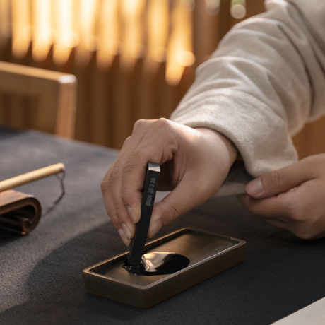 Hand holding a calligraphy brush over gold-leafed paper at Amanyangyun, China.
