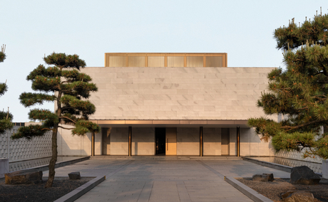 Amanyangyun's main pavilion with angular roof and stone façade at dusk, flanked by manicured evergreen trees.