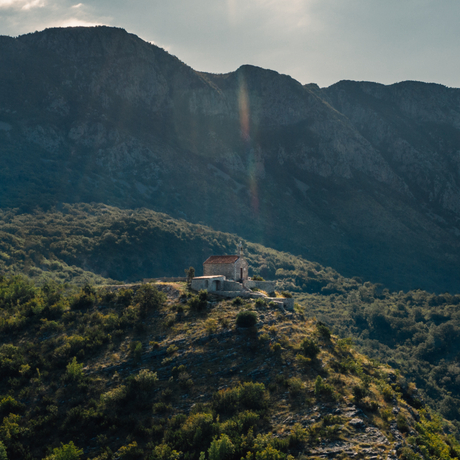 Aman Sveti Stefan set against forested Montenegrin mountains under soft afternoon light.