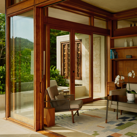 Spacious living room at Amanera with wooden-framed glass doors opening to tropical gardens, featuring warm wood tones and natural light.