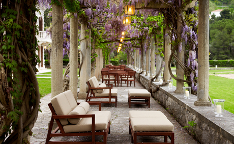Restaurant terrace at Aman Sveti Stefan with stone columns, flowering vines, and lounge seating overlooking gardens, Montenegro.