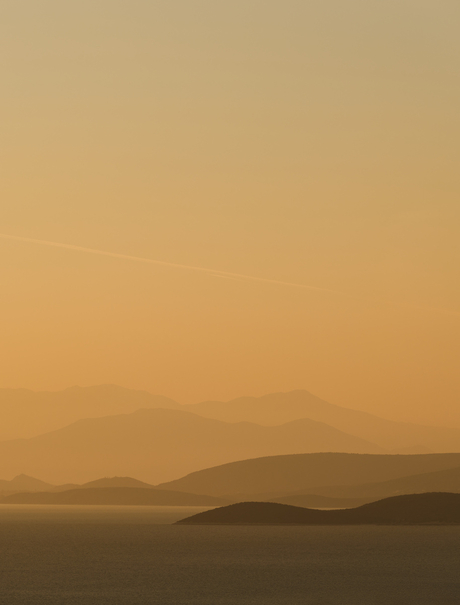 Vista al atardecer desde Amanzoe resort en Grecia, con montañas y agua en tonos cálidos.