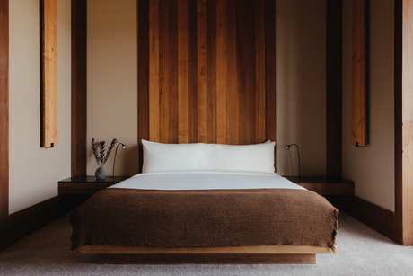 Deluxe Suite bedroom at Amangani with wooden bed frame and white pillows in warm-toned interior.