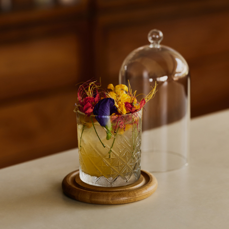 Cocktail with edible flowers under a glass cloche at Amanera bar.
