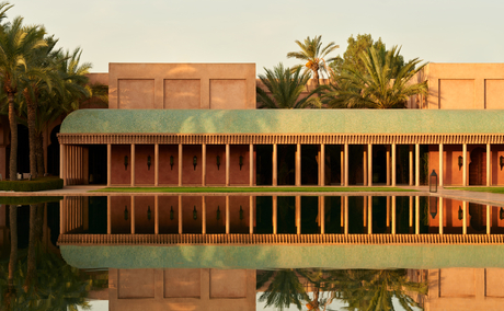 Amanjena's terracotta exterior pavilion reflected in still water, framed by palm trees at dusk.