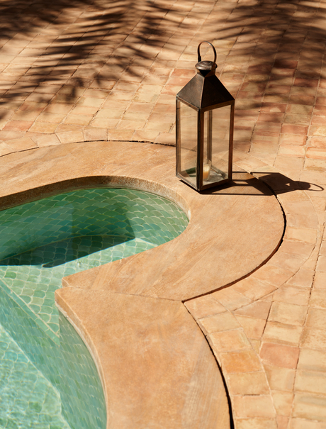Curved plunge pool with turquoise water at Amanjena, with lantern and shadow on sandy terracotta surrounds.