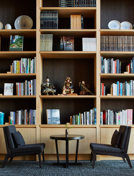 Library at Aman Tokyo with wooden shelving, books, decorative objects and two black chairs at a reading desk.