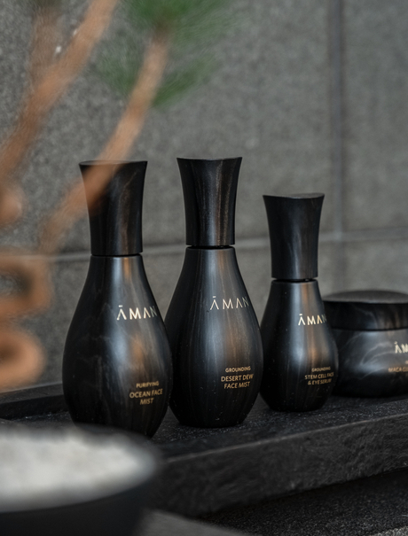 Aman Tokyo skincare bottles arranged on a dark surface with natural light casting shadows.