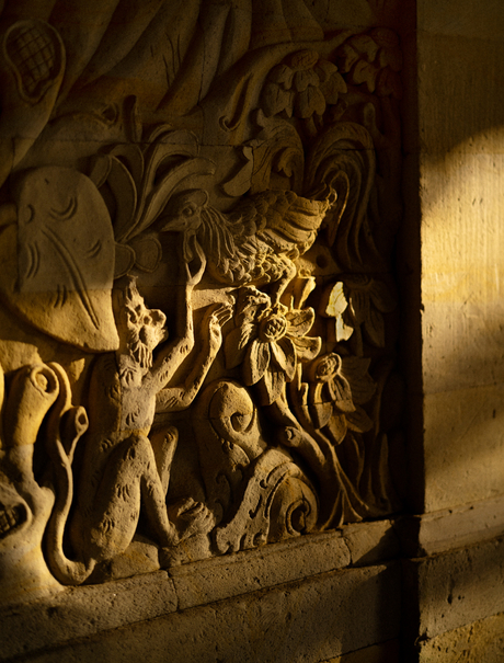 Ornate stone relief carving illuminated by warm light at Amandari resort in Bali, Indonesia.