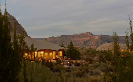 Amangiri camp pavilion glowing at dusk, surrounded by desert landscape and mountains.