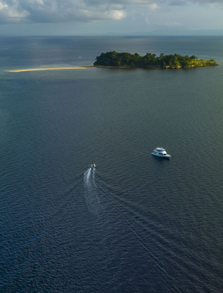 Aerial view of a speedboat approaching a small forested island in Saleh Bay, Sumbawa, Indonesia, where Amanwana is located.