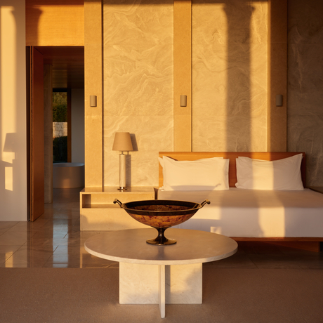Villa bedroom at Amanzoe resort with warm stone walls, platform bed and sculptural bronze vessel.