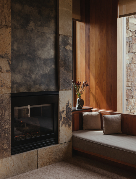 Amangani bedroom with dark stone fireplace, wooden door, and bathtub by window.