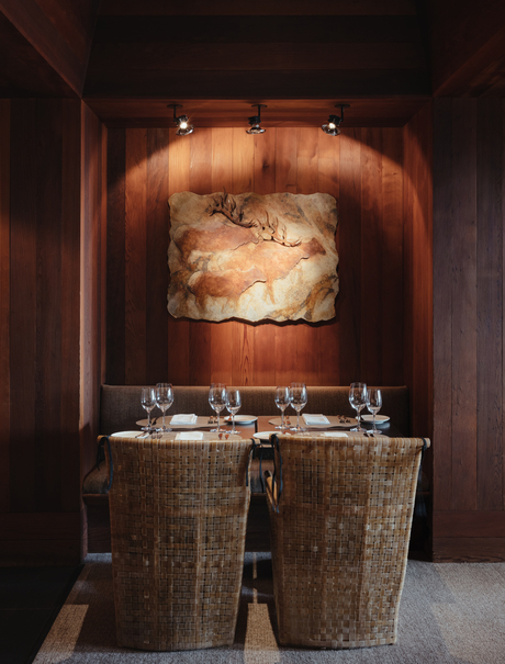 Amangani dining venue with woven chairs facing a warm-lit stone fireplace.