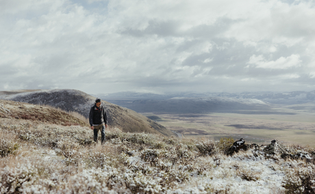 A solitary figure stands on a snow-dusted ridge overlooking vast mountain valleys at Amangani.