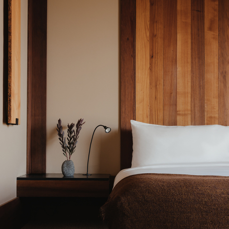 Amangani bedroom with wooden headboard panelling, white pillows and bedside table with lavender arrangement.