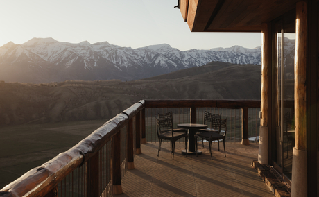 Wooden deck at Amangani with dining table overlooking snow-capped mountains at sunset.