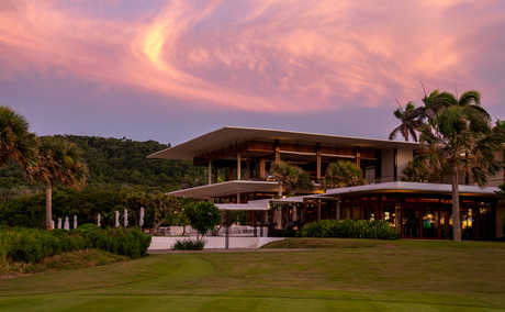 Amanera accommodation at dusk, with warm lights glowing from the wooden structure set against a pink-streaked sky and manicured lawn.
