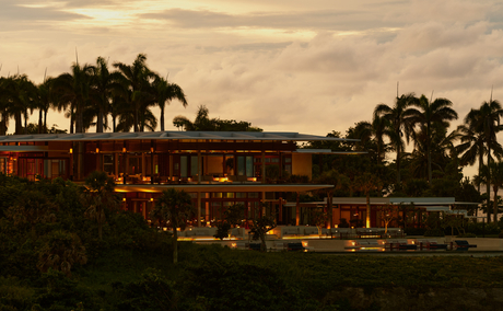 Amanera resort at dusk, warm lights glowing from terracotta buildings beneath palm trees against golden sky.